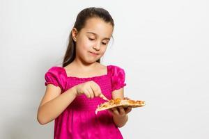 Cute little Indian Asian girl child eating tasty Pizza. Standing isolated over white background. photo