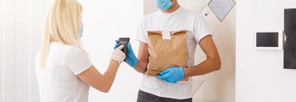 Courier in protective mask delivers parcel, customer in medical gloves receives box. Delivery service under quarantine, disease outbreak, coronavirus covid-19 pandemic conditions. photo