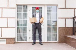 Courier in protective mask and medical gloves delivers takeaway food. Delivery service under quarantine, disease outbreak, coronavirus covid-19 pandemic conditions. photo