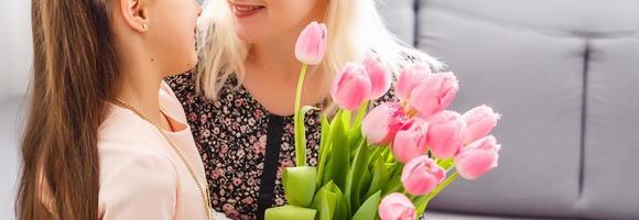 Happy mother's day. Child daughter congratulates mom and gives her flowers tulips. Mum and girl smiling and hugging. Family holiday and togetherness. photo