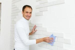 male builder wipes brick tiles on the wall after repair photo