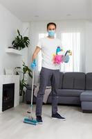 cleaning, health and hygiene concept - indian man wearing protective medical mask for protection from virus disease in gloves with detergent and mop at home photo