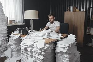 homme au milieu de piles de papiers sur son bureau photo