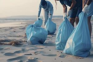 a group of unrecognizable people collecting garbage from the beach in blue bags for the problem of plastic pollution in the environment photo