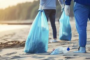 a group of unrecognizable people collecting garbage from the beach in blue bags for the problem of plastic pollution in the environment photo