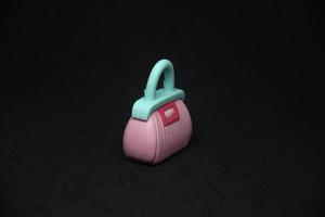 Pink women bag with blue handle shaped eraser stationary tools for office or school supplies. Isolated photo on plain dark black background.