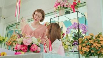 Two young beautiful female florist partners discussing bunch of blossoms arrangement, decorating with lovely ribbons, happy work in colorful flower shop store with blooms, SME business entrepreneur. video