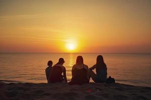 Group of five happy people sits on background of empty sunset beach. Travel or sea vacations concept photo