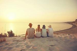 Group of five happy people sits on background of empty sunset beach. Travel or sea vacations concept photo