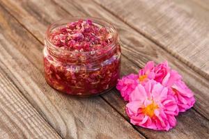 Jam jar of rose petals on wooden background. photo