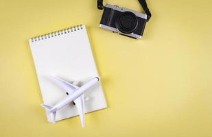 flat lay of blank page opened notebook, airplane model  and camera on yellow  background with copy space. Travel, photo and memory concept.