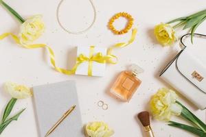 Workplace with a notebook and a pen, yellow tulips, a bracelet, a women's handbag, eau de toilette on a light background. Flat composition for bloggers, magazines, social media and artists. Top view photo