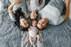 Happy family with two small children are lying resting on the bed and smiling. Top view photo