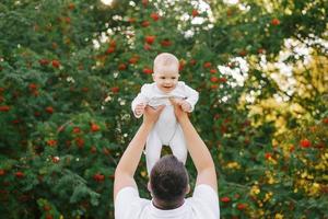 un padre obras de teatro con su hijo en el parque en el verano. un hombre sostiene un pequeño chico arriba en su brazos foto