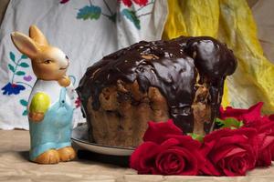 Beautiful Easter background. Chocolate cake with red roses and an Easter bunny on the background of an embroidered shirt. photo