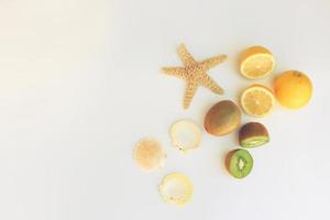 Lemons, kiwi fruit and starfish, shells, on white background. Toned image. Top view. photo