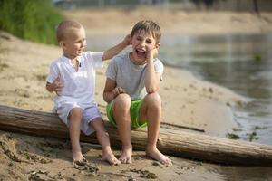 dos hermanos, el mayor y el más joven, son jugando por el río. niños en el arenoso apuntalar hablar y complacer. foto