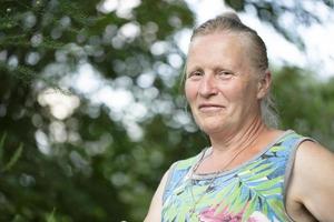 Portrait of an elderly fair-haired woman of normal appearance against a background of greenery. photo