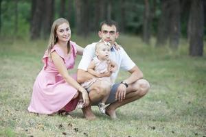 marido, esposa y su pequeño hija para un caminar en el parque. contento papá y mamá con su un año de edad hija son mirando a el cámara. foto