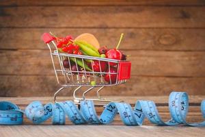 Shopping cart with fruits, berries and tape line on old wood background. Toned image.