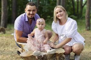 marido, esposa y su pequeño hija. familia retrato en naturaleza. mamá y papá son participación el bebé en su brazos. un joven familia con niños es mirando dentro el cámara. foto