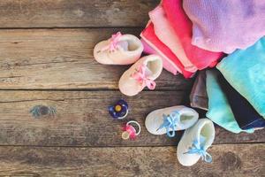 Baby shoes, clothing and pacifiers pink and blue on the old wooden background. Toned image. photo