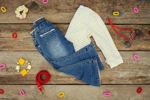 Children's clothing and accessories jeans, hair clips, blouse, warm vest on old wooden background. Top view. photo