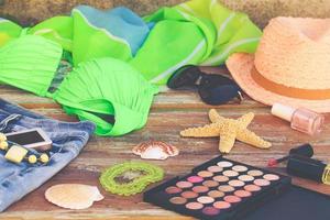 Summer women's clothing and accessories hat, bathing suit, denim shorts, cosmetics, pareo, sunglasses, mobile phone, headphones, shells. Toned image. Top view. photo