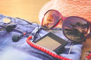 Summer women's accessories red sunglasses, beads, denim shorts, mobile phone, headphones, sun hat. Toned image photo