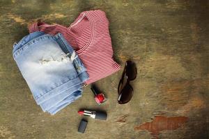 Summer women's clothing and accessories t-shirt, jeans, lipstick, nail polish, belt, sunglasses. Top view. photo