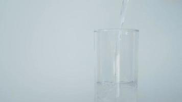 derramando purificado água para dentro uma vidro do água em uma branco fundo. video