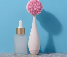 White glass bottle with a pipette and a plastic facial brush on a blue background photo