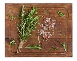 Twigs and leaves of rosemary, dry fruits of red, black and allspice and salt on a wooden cutting board, top view photo