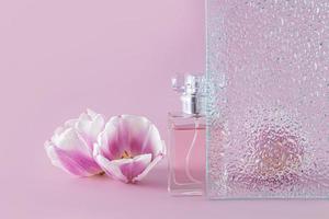 creative composition with a beautiful bottle of women's perfume, embossed glass and delicate spring flowers. front view. lilac background. photo