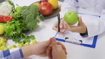 a dietista médico conta dela paciente sobre saudável comendo com uma vegetal dieta. uma fêmea dietista conta dela paciente uma dieta Lista consistindo do legumes e frutas. video
