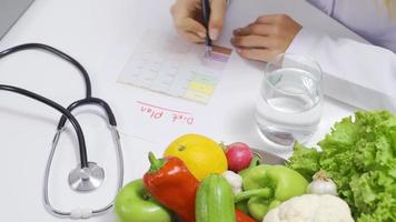 Nutritionist woman prepares diet plan for healthy life at table. Nutritionist woman writing diet plan on table full of fruits and vegetables. video