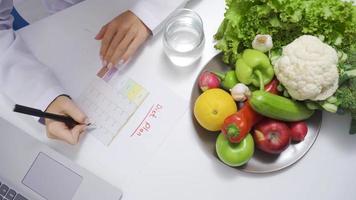 fêmea nutricionista usando computador portátil dentro escritório. nutricionista preparando dieta Lista com saudável frutas e legumes. video