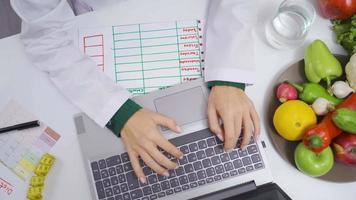 A nutritionist prepares a diet plan at her desk. A dietitian working for a healthy life prepared diet plans with vegetables and fruits on her table. video