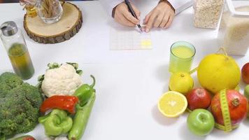 The dietitian prepares a proper nutrition diet about healthy foods. Working at a table full of healthy foods, a dietitian prepares a diet program. video