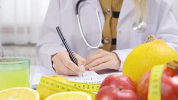 A dietitian working at a fruit-filled table prepares a healthy menu. Dietitian woman with tape measure and organic fruits on her desk works, prepares plans and programs. video