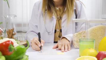 A nutritionist who cares about healthy life and nutrition, prepares a diet program for her patients. Working at a table full of healthy foods, a dietitian prepares a diet program. video