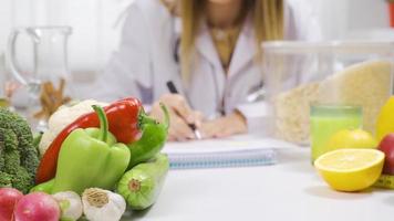 voedingsdeskundige vrouw benadrukkend welzijn en voeding. werken Bij een tafel vol van fruit en groenten, een diëtist bereidt zich voor een gezond eetpatroon programma. video