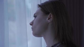 Lonely woman looking out window from home thoughtful and unhappy. The woman looking out the window is thoughtful and alone in the house. video