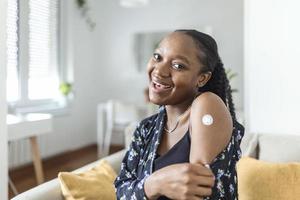 Portrait of a female smiling after getting a vaccine. Woman holding down her shirt sleeve and showing her arm with bandage after receiving vaccination. photo