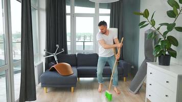 Man cleaning the house, having fun dancing and singing with a broom. video