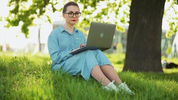 ocupado atractivo mujer trabajando en el ordenador portátil mientras sentado en césped en ciudad parque