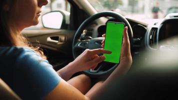 hembra conductor utilizando un teléfono inteligente dentro el coche. chromakey teléfono inteligente con verde