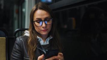 Publique transport à nuit. femme dans des lunettes dans tram en utilisant téléphone intelligent video