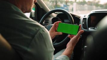 masculino conductor utilizando un teléfono inteligente dentro el coche. chromakey teléfono inteligente con verde