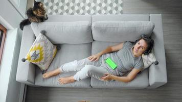 Relaxed woman in headphones with smartphone with green mock-up screen video